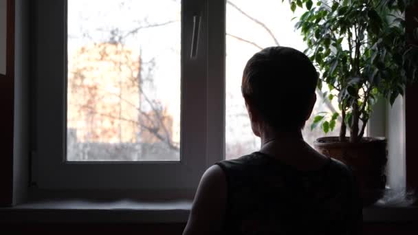 Vista trasera de la abuela mirando por la ventana. Concepto. La anciana mira por la ventana esperando ver a alguien. Mujer mayor mira lo que está sucediendo en la calle — Vídeo de stock