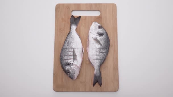 Two raw fish on wooden board on white background. Action. Delicious two butchered fish on board before baking on isolated background — Stock Video