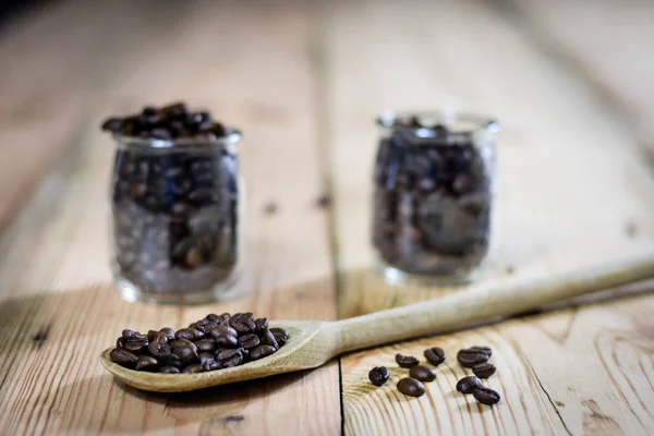 Granos de café en tarro y cuchara de madera, mesa de madera —  Fotos de Stock