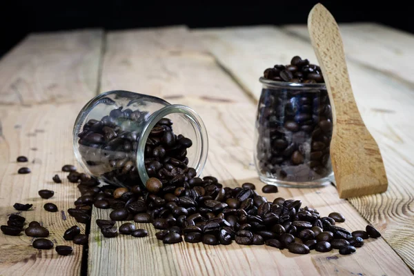 Granos de café en tarro y cuchara de madera, mesa de madera — Foto de Stock