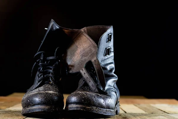 Błotniste stare buty wojskowe. Kolor czarny, brudne podeszwy. Drewniany stół — Zdjęcie stockowe