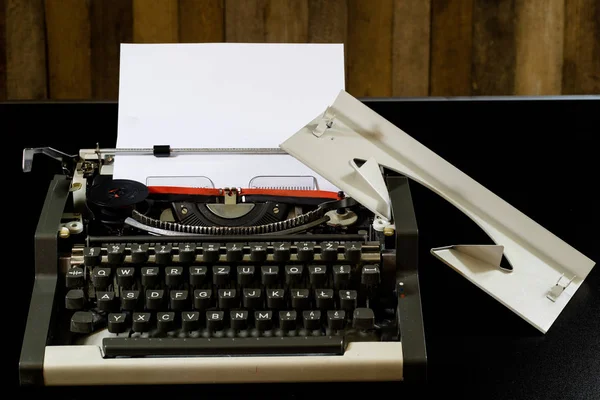 Máquina de escribir en la mesa negra. Tarjeta blanca en blanco. Pared de b áspero —  Fotos de Stock