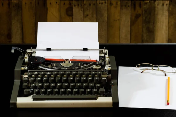 Máquina de escribir en la mesa negra. Tarjeta blanca en blanco. Pared de b áspero — Foto de Stock