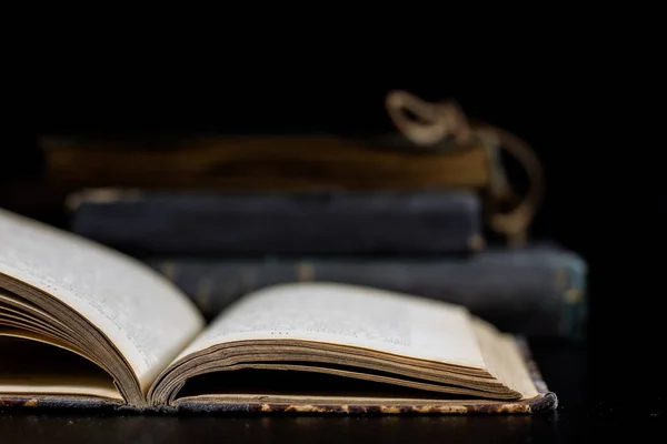 Siyah bir masanın üzerinde yatan bir eski kitap. Arka planda bir yığın 