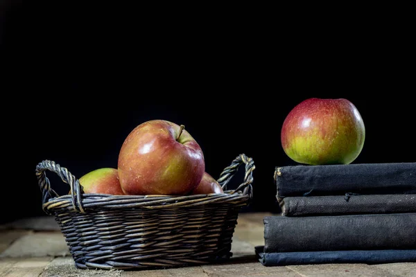 Tasty apples in basket on kitchen table. Old books lie next to a — Stock Photo, Image