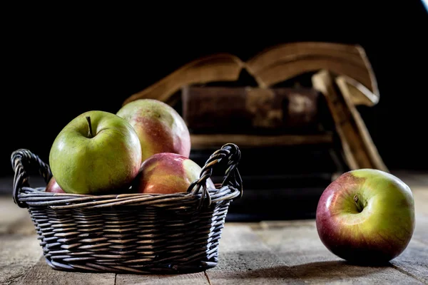 Tasty apples in basket on kitchen table. Old books lie next to a — Stock Photo, Image