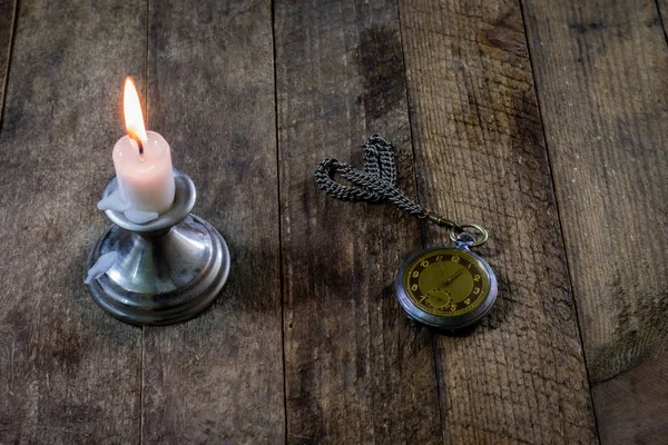 Candela accesa e vecchio orologio su un tavolo di legno. Tempo di scorrimento e — Foto Stock