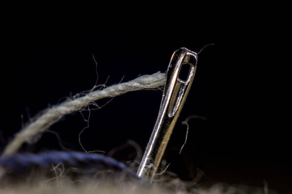 The ear of a sewing needle with a thread. The thread is threaded