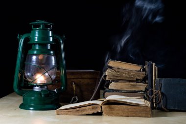 Eski yağ lambası ve masanın üzerinde yatan kitaplar. Eski s bir alev