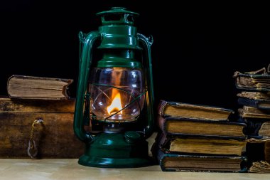 Eski yağ lambası ve masanın üzerinde yatan kitaplar. Eski s bir alev