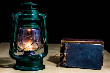 Eski yağ lambası ve masanın üzerinde yatan kitaplar. Eski s bir alev