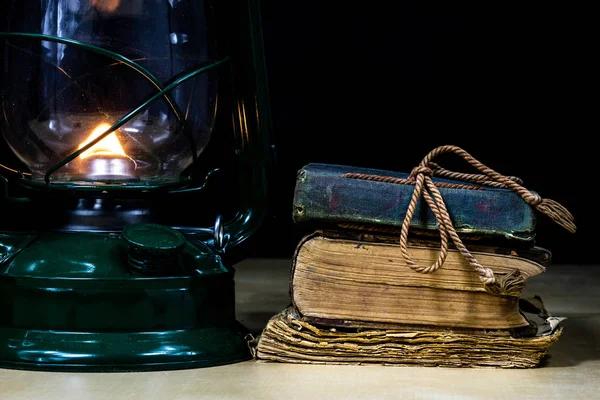 Old oil lamp and books lying on the table. A flame from an old s — Stock Photo, Image