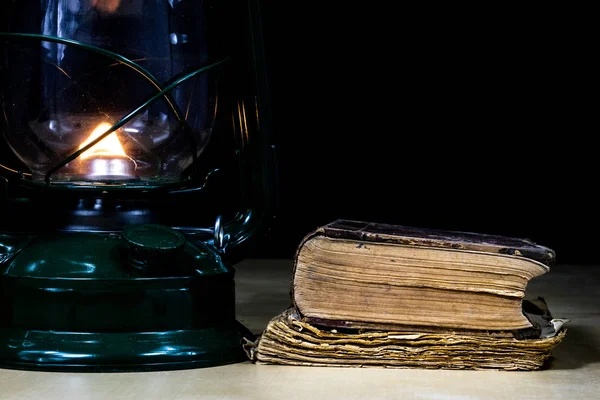 Eski yağ lambası ve masanın üzerinde yatan kitaplar. Eski s bir alev