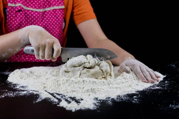 Amassar a massa de farinha em uma mesa preta em uma padaria. Mãos de padeiro prepa — Fotografia de Stock