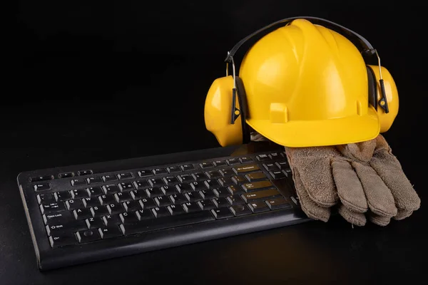 Construction helmet, work gloves on the computer keyboard. Work