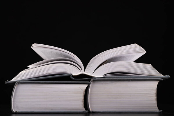 An open thick book on a stack of other books. Extensive books preparation for reading and analysis. Dark background.