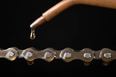 Oiling the bicycle chain with an oiler. Care of the bicycle's drive system. Dark background. clipart