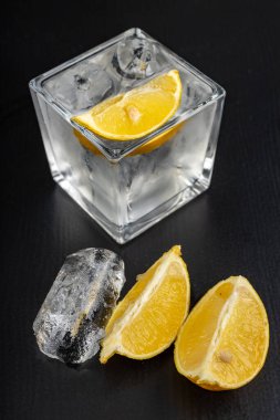 Cam bir kabın içinde soğuk bir içecek. Karanlık bir masada buzlu ve limonlu su. Siyah arkaplan.