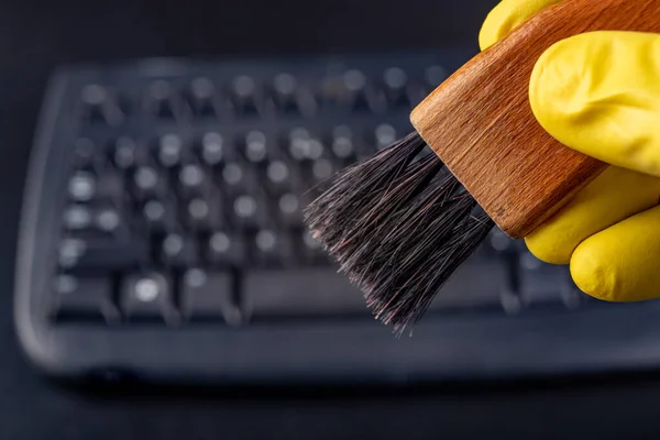 Cleaning the keyboard from dust and dirt with a brush. Maintenance and cleaning of computer hardware. Dark background.