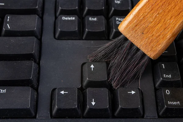 Cleaning the keyboard from dust and dirt with a brush. Maintenance and cleaning of computer hardware. Dark background.