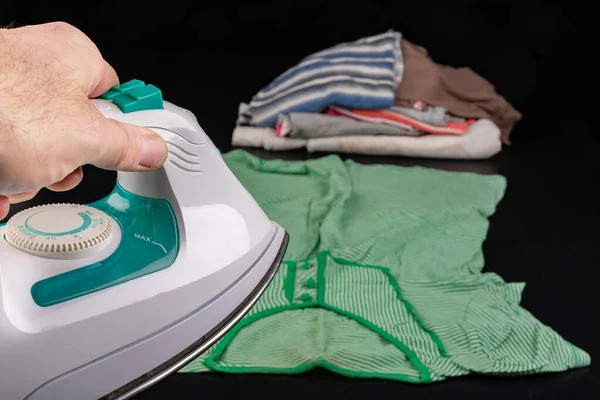 Ironing clothes at home. Domestic work done mostly by women. Dark background.