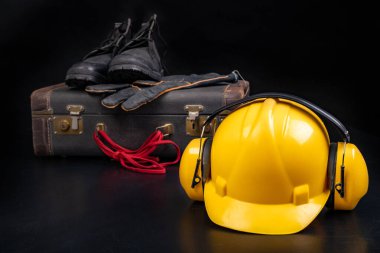 Koruyucu kask, bavul ve iş ayakkabıları. Üretim işçisi için giysi. Koyu arkaplan.