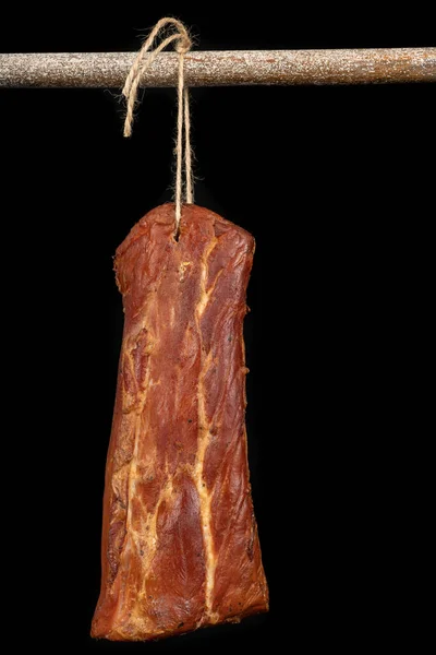 A tasty piece of smoked pork loin hung on a jute string. Stocks in the home pantry. Dark background.