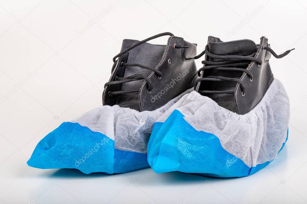 Black work shoes in protectors. Virus protection during pandemic times. Light background.