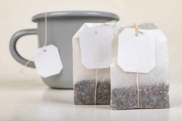 A bag of tasty tea and a mug. Tea leaves packed in a brewing bag. Light background.