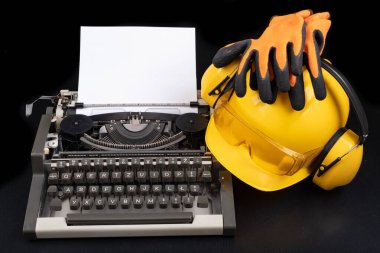 Eski bir daktiloda bir miğfer. Ofisteki mühendis için aksesuarlar. Koyu arkaplan.