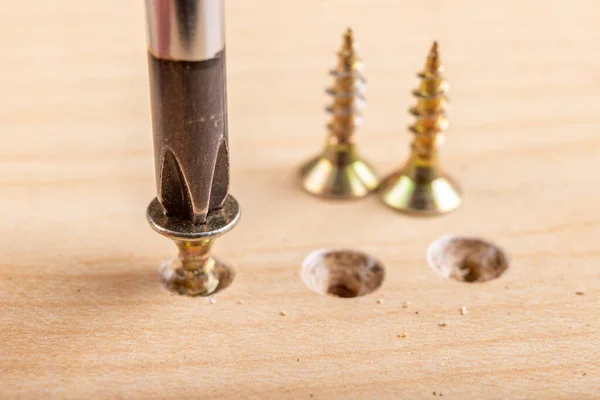 Screwing metal screws into chipboard for furniture construction. Small carpentry work in the home workshop. Light background.