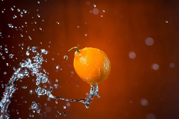 Лимон и брызги воды на оранжевом фоне — стоковое фото