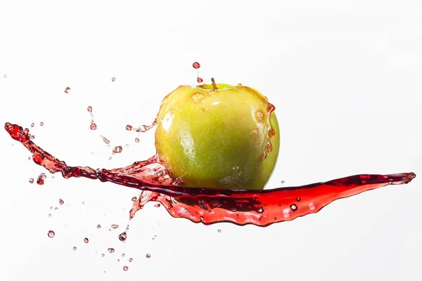 Зеленое яблоко и брызги красного сока на белом фоне — стоковое фото