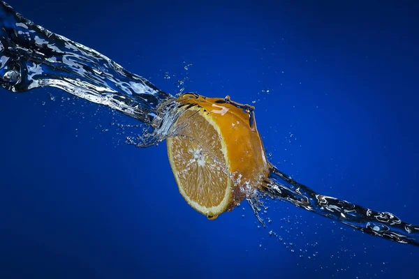 Mitad de naranja y salpicadura de agua sobre fondo azul —  Fotos de Stock