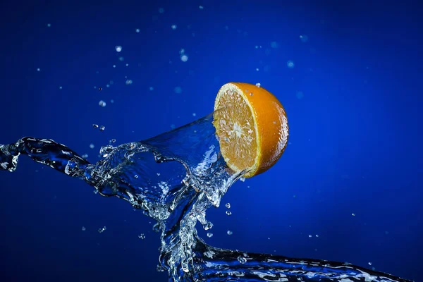 Mitad de naranja y salpicadura de agua sobre fondo azul —  Fotos de Stock