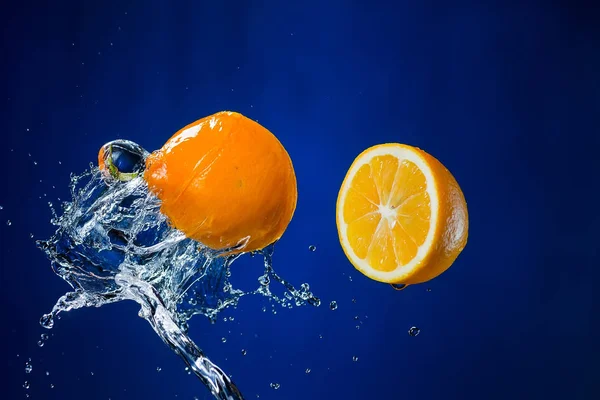 Dos mitades de naranja y salpicadura de agua sobre fondo azul —  Fotos de Stock