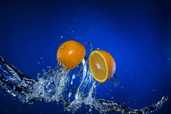 Dos mitades de naranja y salpicadura de agua sobre fondo azul —  Fotos de Stock