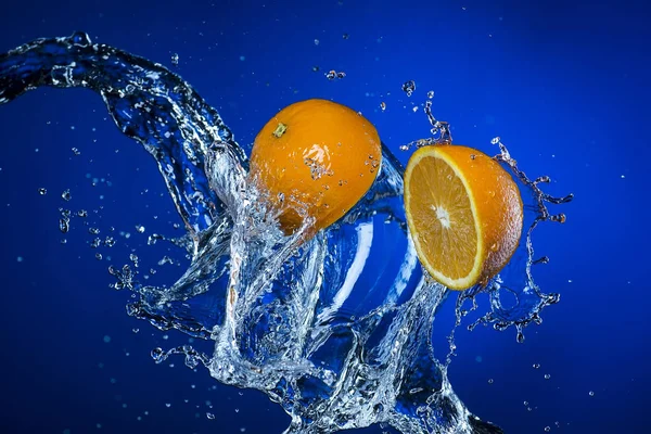 Dos mitades de naranja y salpicadura de agua sobre fondo azul —  Fotos de Stock