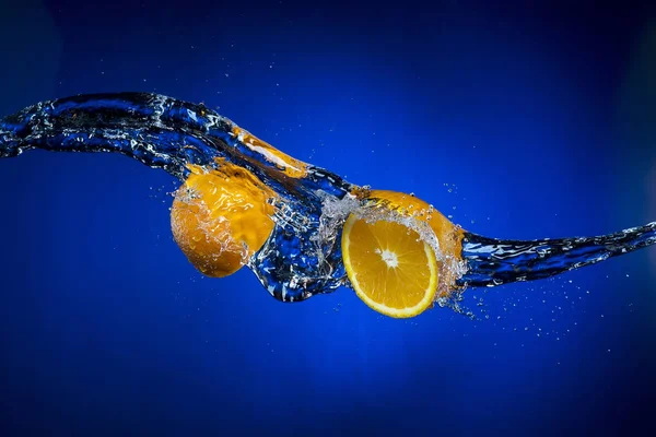 Dos mitades de naranja y salpicadura de agua sobre fondo azul —  Fotos de Stock