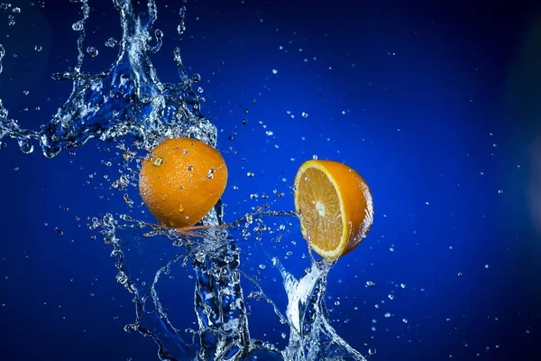 Dos mitades de naranja y salpicadura de agua sobre fondo azul —  Fotos de Stock