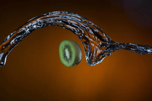 Mitad de kiwi y salpicadura de agua sobre fondo naranja —  Fotos de Stock