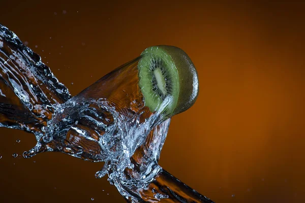 Mitad de kiwi y salpicadura de agua sobre fondo naranja —  Fotos de Stock