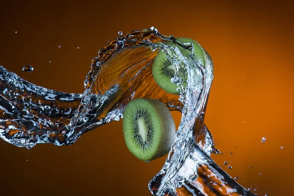 Две половинки киви и брызги воды на оранжевом фоне — стоковое фото