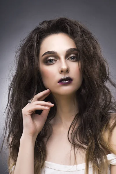 Retrato de belleza de la joven en una camiseta blanca con un maquillaje de vanguardia y un pelo que fluye sobre un fondo gris — Foto de Stock