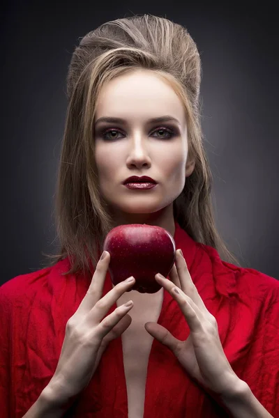Retrato da jovem mulher em um lenço vermelho com um penteado de vanguarda que mantém na mão maçã vermelha em um fundo cinza — Fotografia de Stock