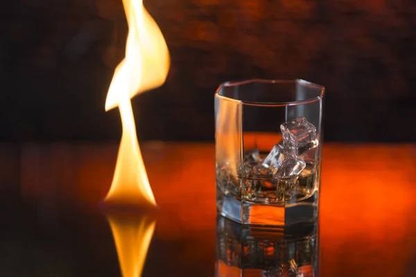 Bicchiere di whisky con ghiaccio su fondo rosso e fuoco — Foto Stock