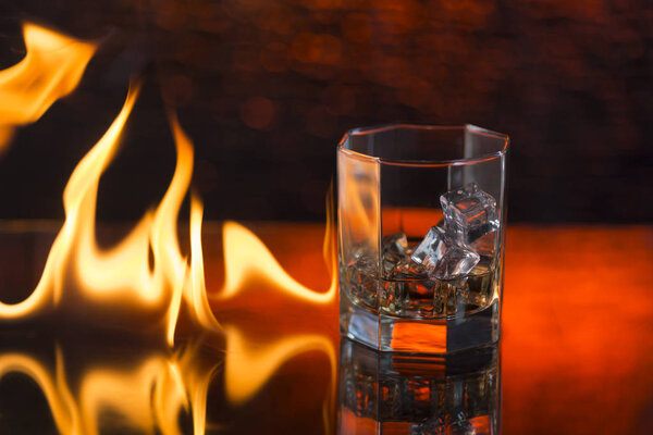 glass of whisky with ice on a red background and fire