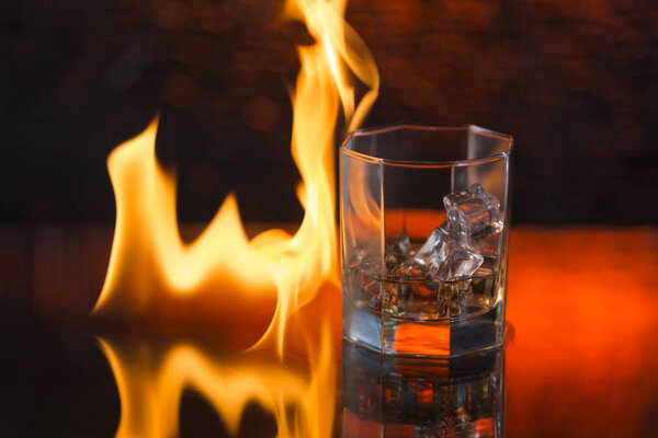 glass of whisky with ice on a red background and fire