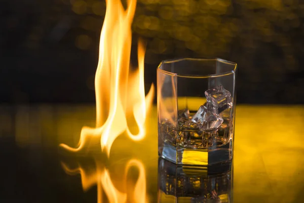 Glass of whisky with ice on a black background and fire flames — Stock Photo, Image