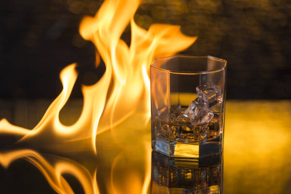 glass of whisky with ice on a black background and fire flames